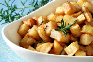 Roasted potatoes with fresh rosemary in white serving bowl.